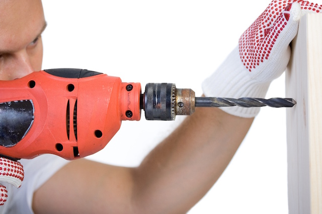Man holding a drill on a peace of wood plank